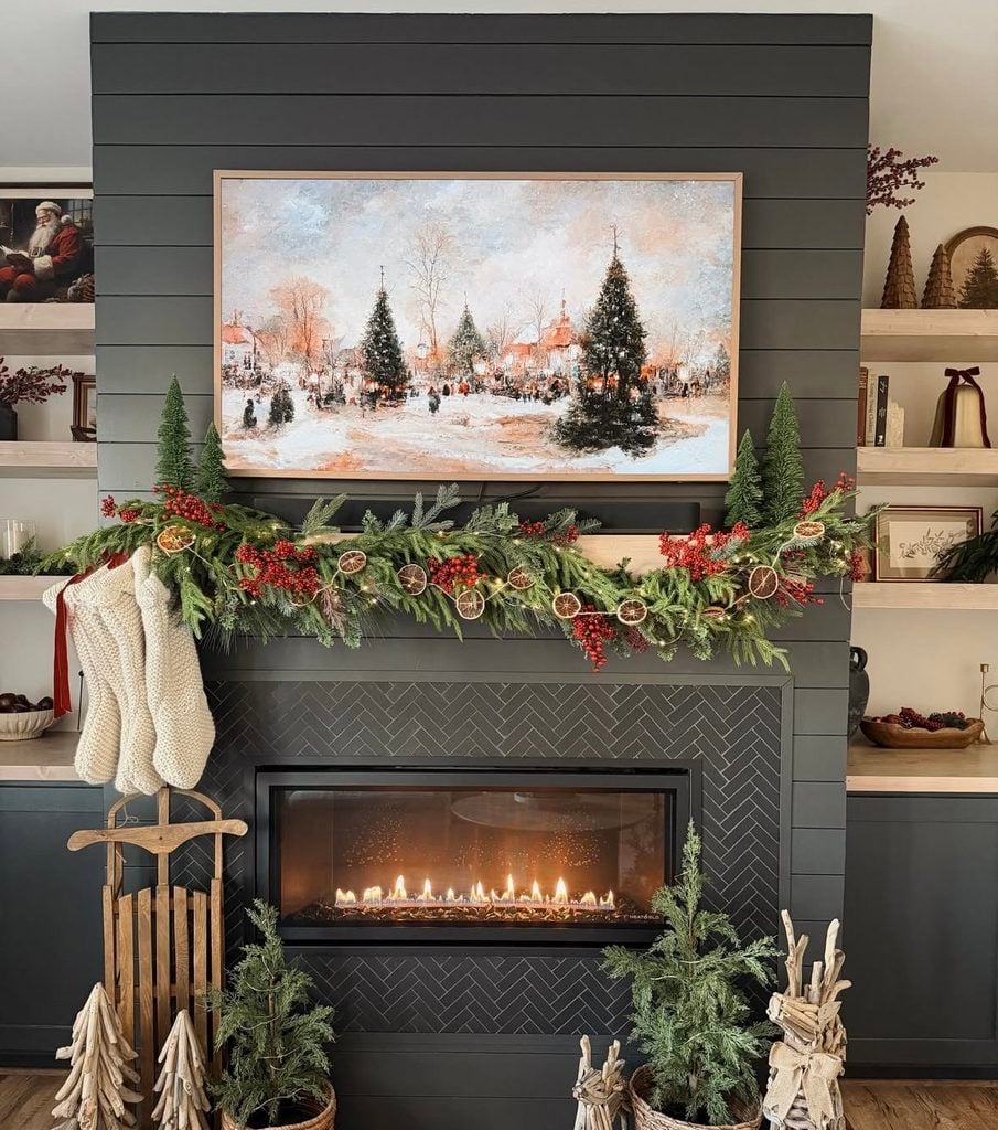 Dark fireplace mantel decorated for Christmas with greenery, stockings, candles, and warm seasonal accents.