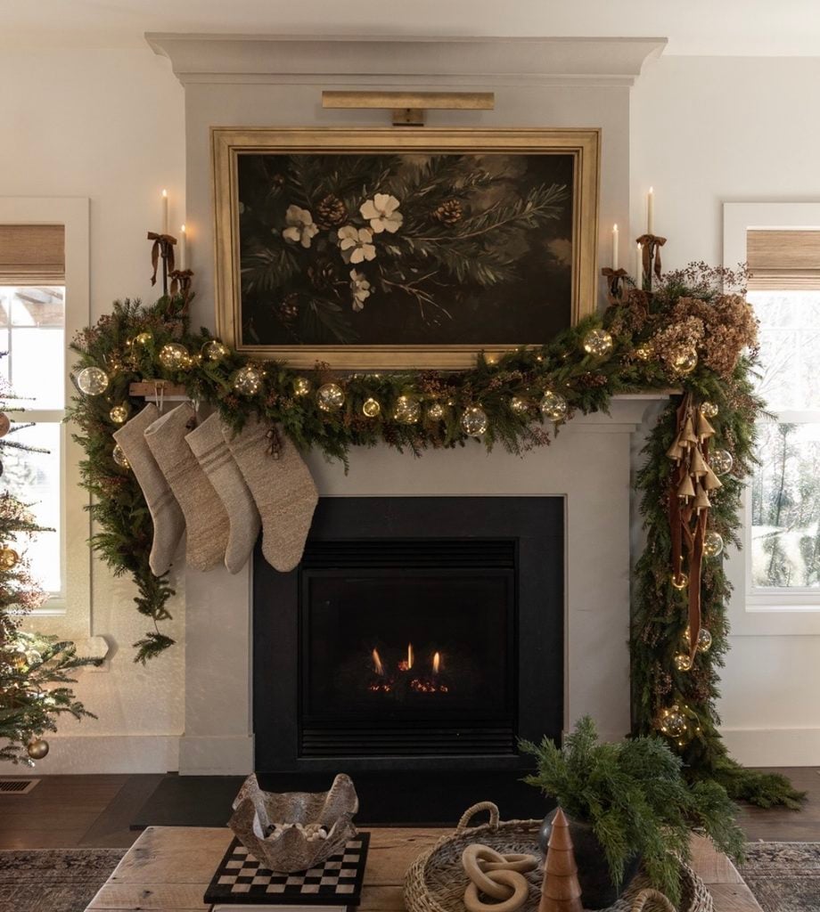 Christmas fireplace mantel with a glowing fire, greenery, stockings, candles, and cozy holiday decorations.
