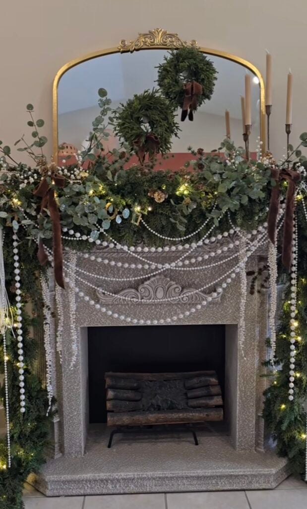Lush green Christmas mantel with pearl accents and layered elegant holiday decor.