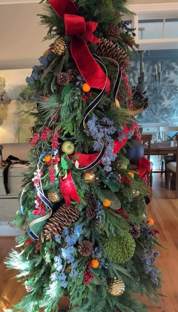 Ralph Lauren Christmas tree decorated with red velvet ribbon, navy ribbon, pine cones, red berries, blue berry accents, gold ornaments, fresh greenery, and natural woodland textures.