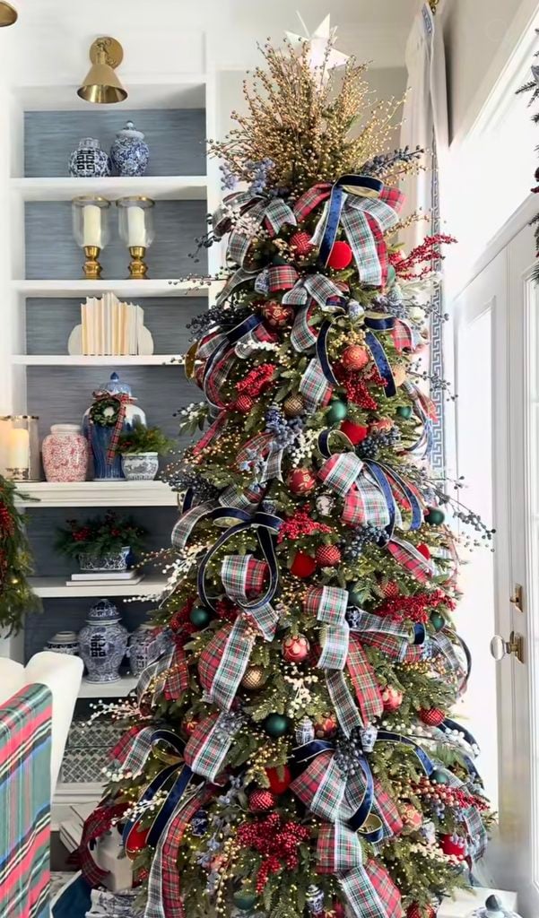 Ralph Lauren Christmas tree with layers of tartan plaid ribbon, navy velvet ribbon, red berries, green and red ornaments, metallic accents, and blue-and-white porcelain decor nearby.