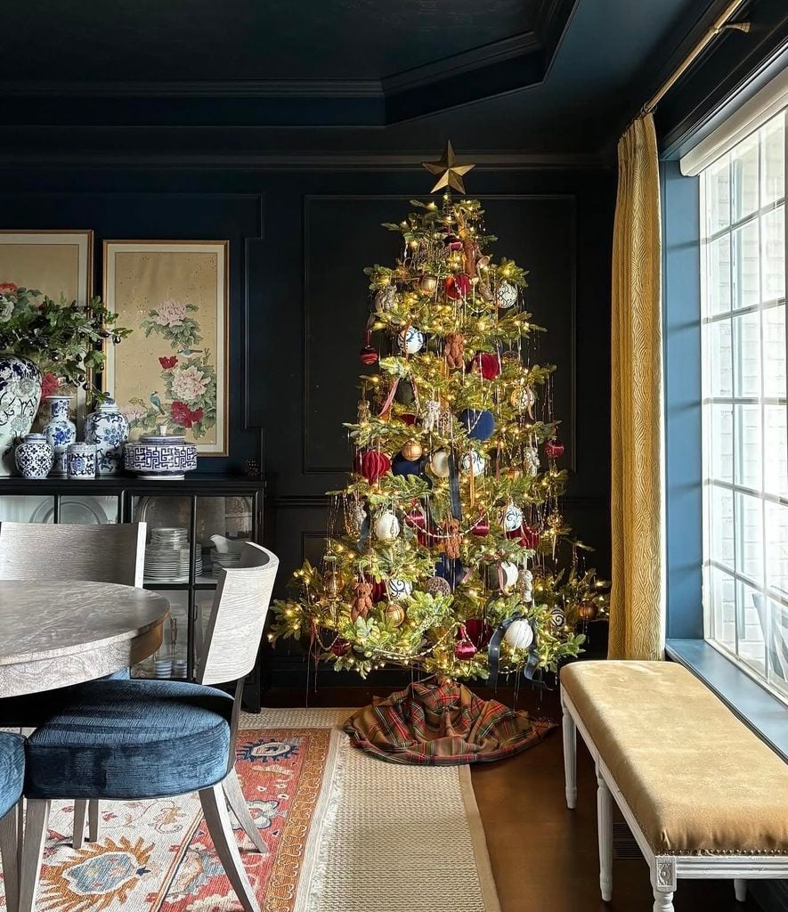 Ralph Lauren-inspired Christmas tree in a dark dining room with red, navy, gold, and white ornaments, hanging gold details, blue-and-white porcelain accents, and a gold star topper.