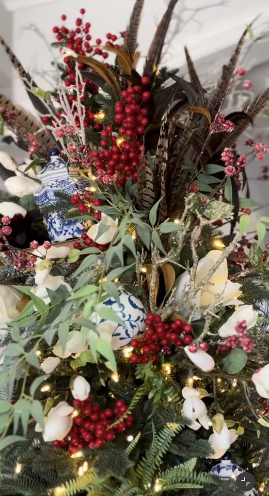 Close-up of a Ralph Lauren Christmas tree topper with pheasant feathers, red berries, greenery, blue-and-white porcelain ornaments, and warm holiday lights.