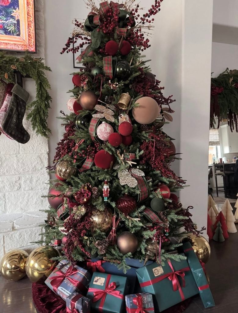 Ralph Lauren Christmas tree decorated with burgundy velvet ornaments, red berry sprays, tartan plaid ribbon, deep green and bronze ornaments, gold accents, and wrapped gifts in rich green and red tones beneath the tree.