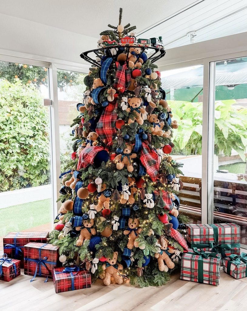 Playful Ralph Lauren Christmas tree decorated with teddy bears, tartan ribbon, navy and red ornaments, a toy train around the top, and plaid-wrapped presents.