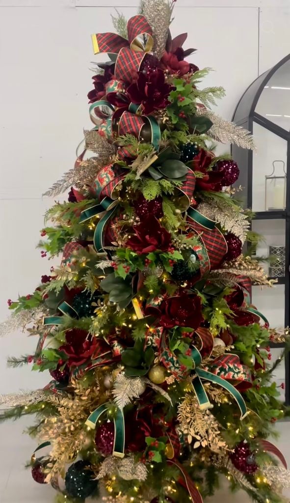 Ralph Lauren Christmas tree topped with layered tartan and green ribbon, burgundy florals, holly, metallic foliage, velvet ornaments, and warm holiday lights.