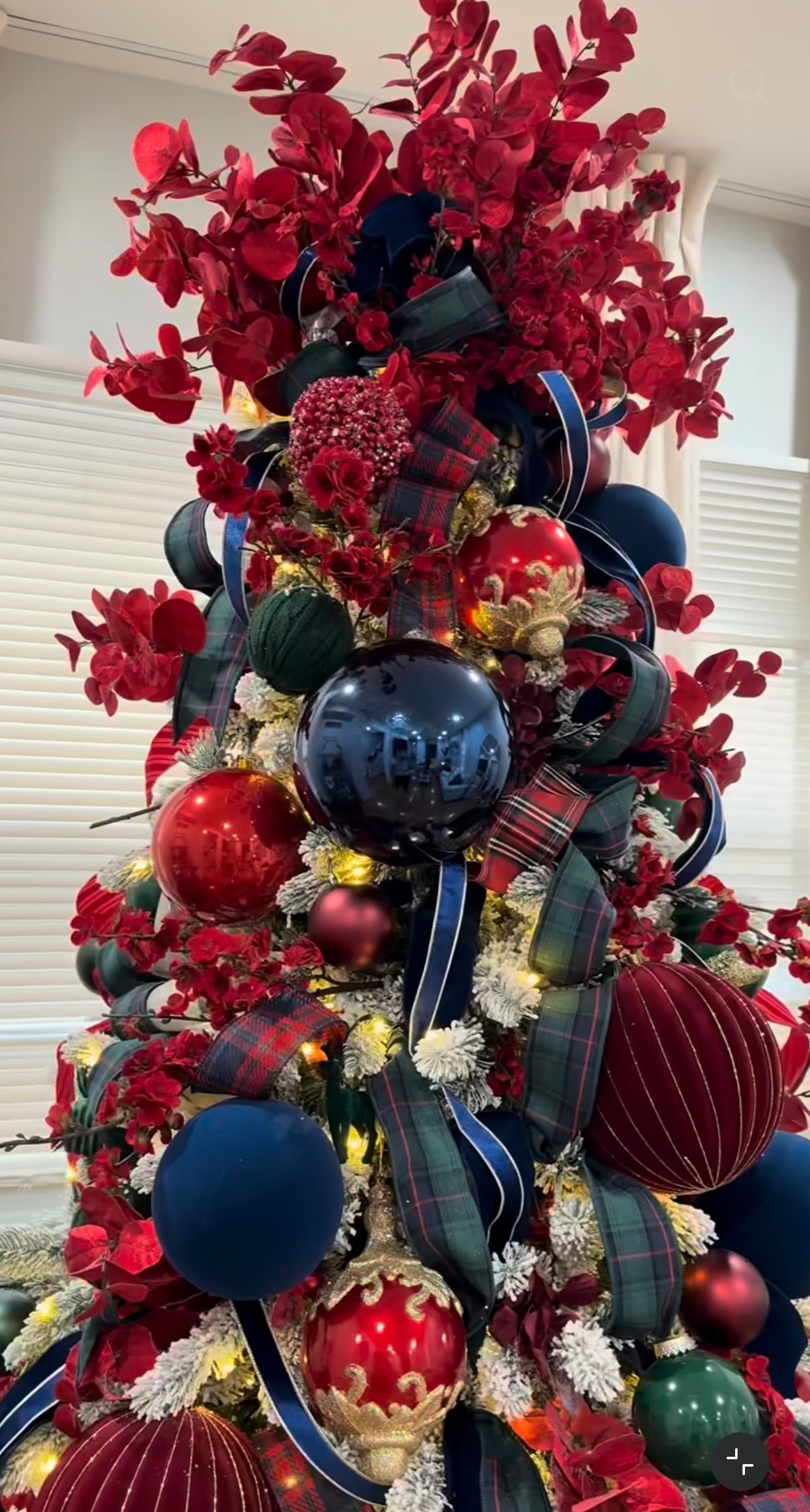 Ralph Lauren Christmas tree decorated with oversized red and navy ornaments, tartan ribbon, burgundy velvet accents, red florals, and rich jewel-toned decorations.