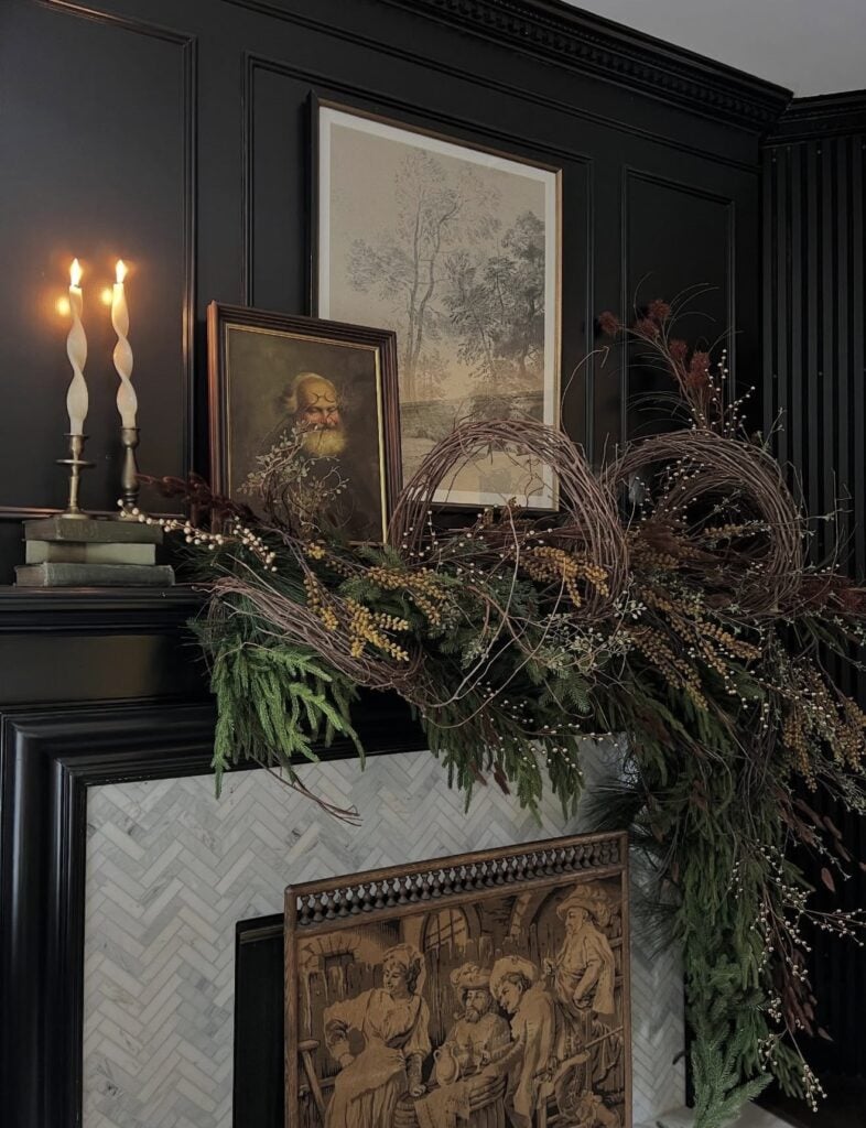 Classic Ralph Lauren-inspired Christmas mantel with natural elements of greenery and sticks with candles and portraits on the fireplace mantel