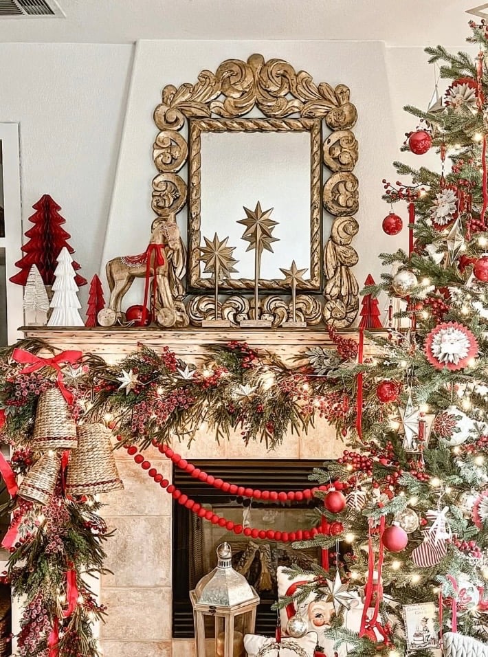 Styled Christmas fireplace mantel with greenery, candles, stockings, and decorative accents arranged at varying heights.