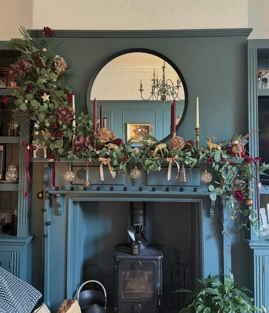 Unique Christmas fireplace mantel styled with layered greenery, unexpected seasonal decorations, and collected holiday details.