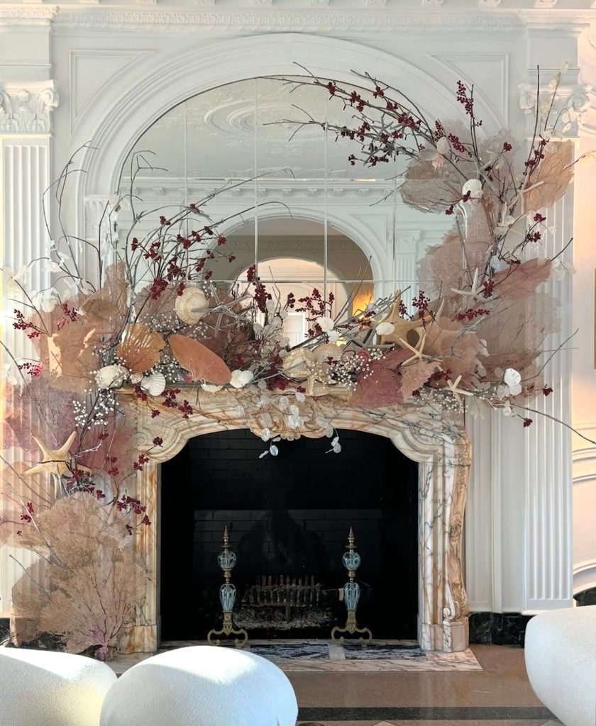 Neutral Christmas mantel with sculptural wave-style greenery, soft seasonal accents, and an elegant modern fireplace display.