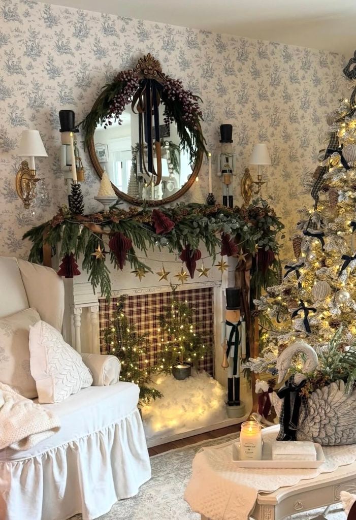 Close-up of a Christmas fireplace mantel in a living room decorated with greenery, candles, and layered holiday accents.