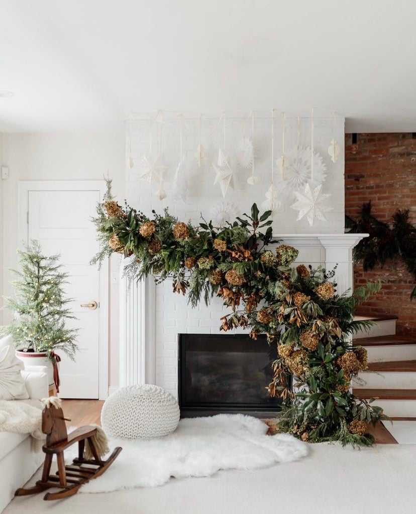 Neutral Christmas fireplace mantel decorated with layered greenery, stockings, candles, and soft natural holiday accents.