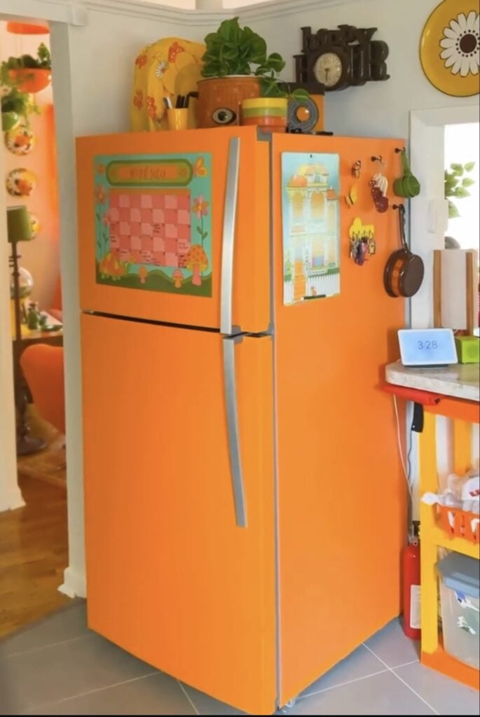 Bright orange refrigerator styled as a bold, colorful statement piece in a retro-inspired kitchen.