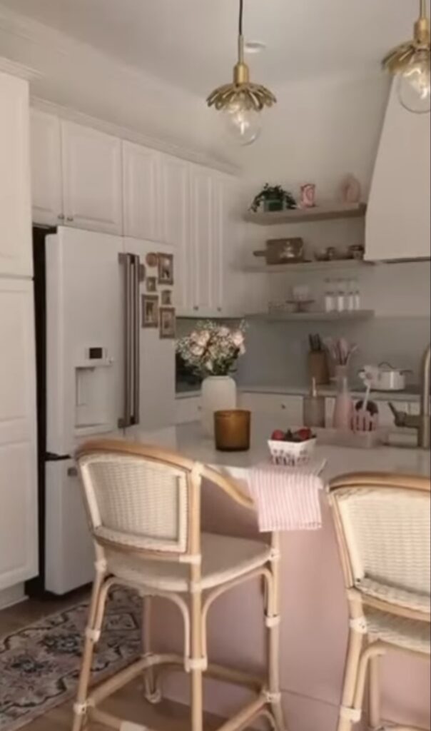 White refrigerator in a soft pink and white kitchen with a small collection of gold-framed photos displayed as a fridge gallery wall.