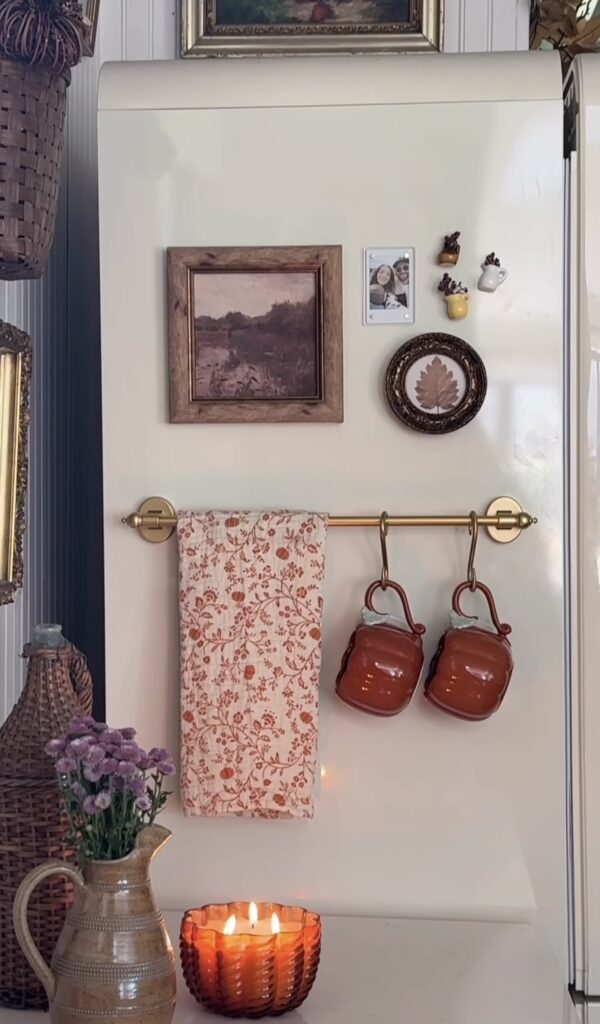 Cozy fridge gallery wall on a cream refrigerator with framed landscape art, a family photo, tiny flower vases, botanical art, a brass towel rod and hanging mugs.