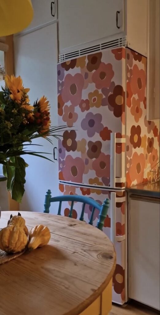 Refrigerator covered in oversized retro floral wallpaper in orange, pink and purple.