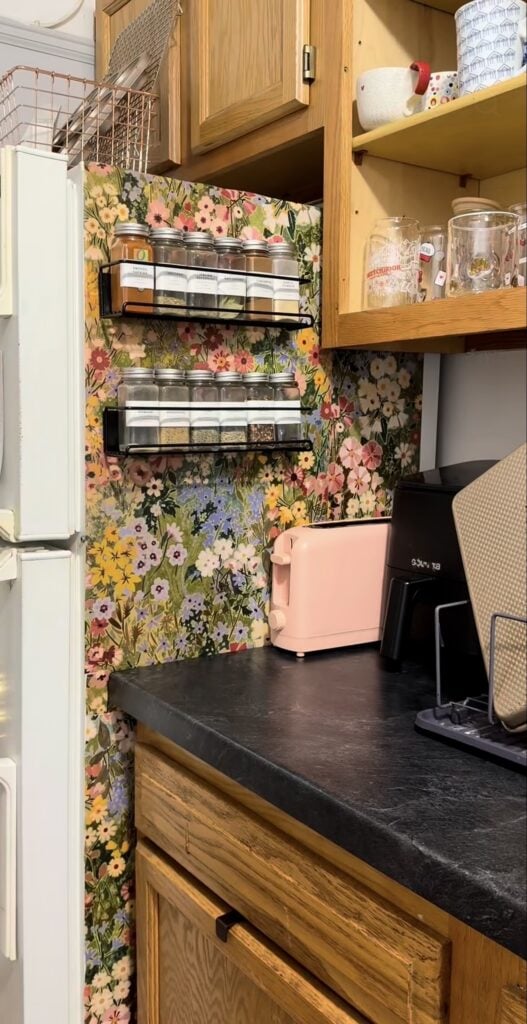 Side of a refrigerator covered in colorful floral wallpaper with two mounted spice racks.
