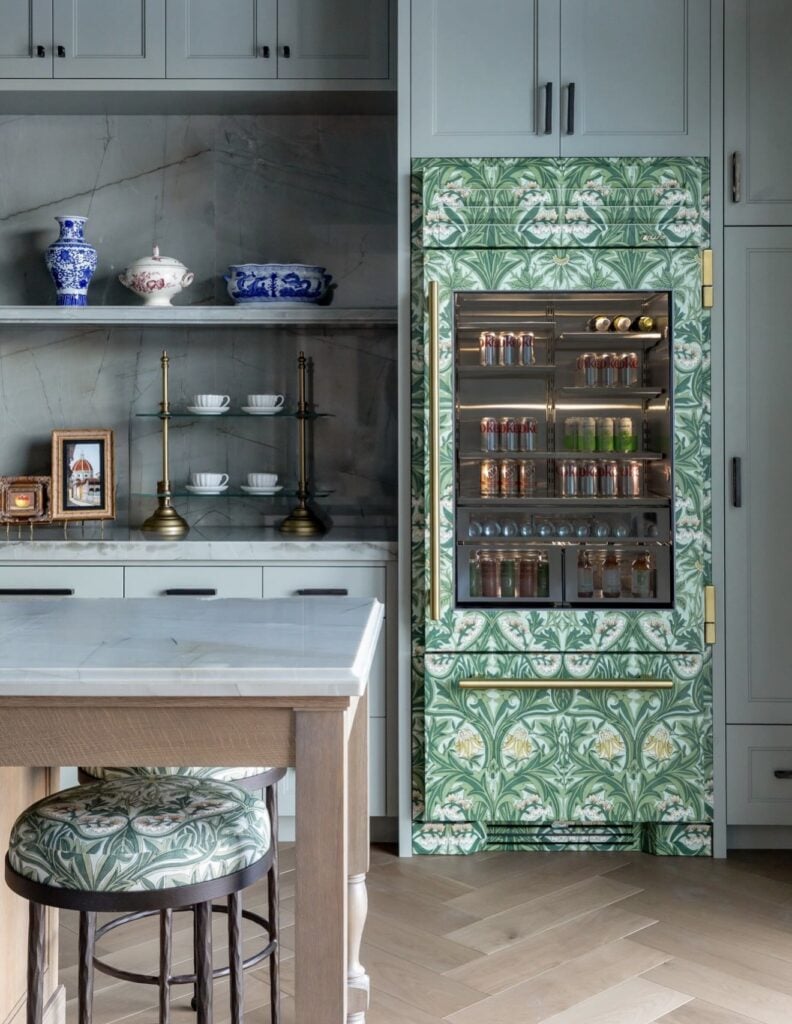 Built-in refrigerator with green botanical wallpaper, brass hardware and a glass-front door in an elegant kitchen.