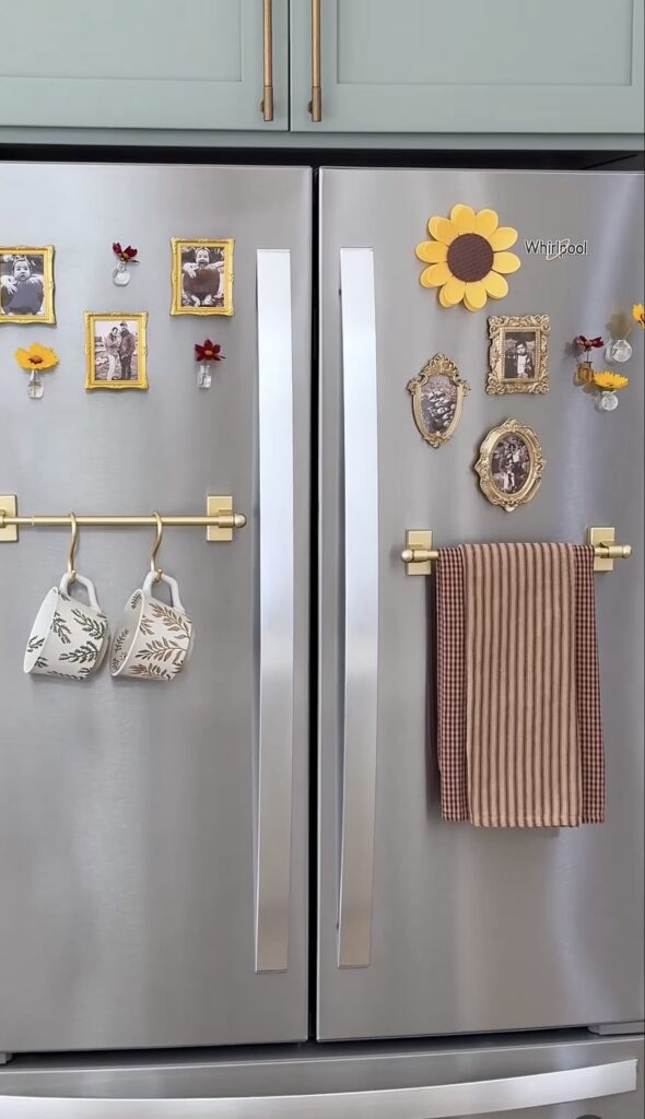 Whimsical fridge gallery wall on a stainless steel refrigerator with ornate family photo frames, miniature flower vases, sunflower decor, brass towel rods and hanging mugs.
