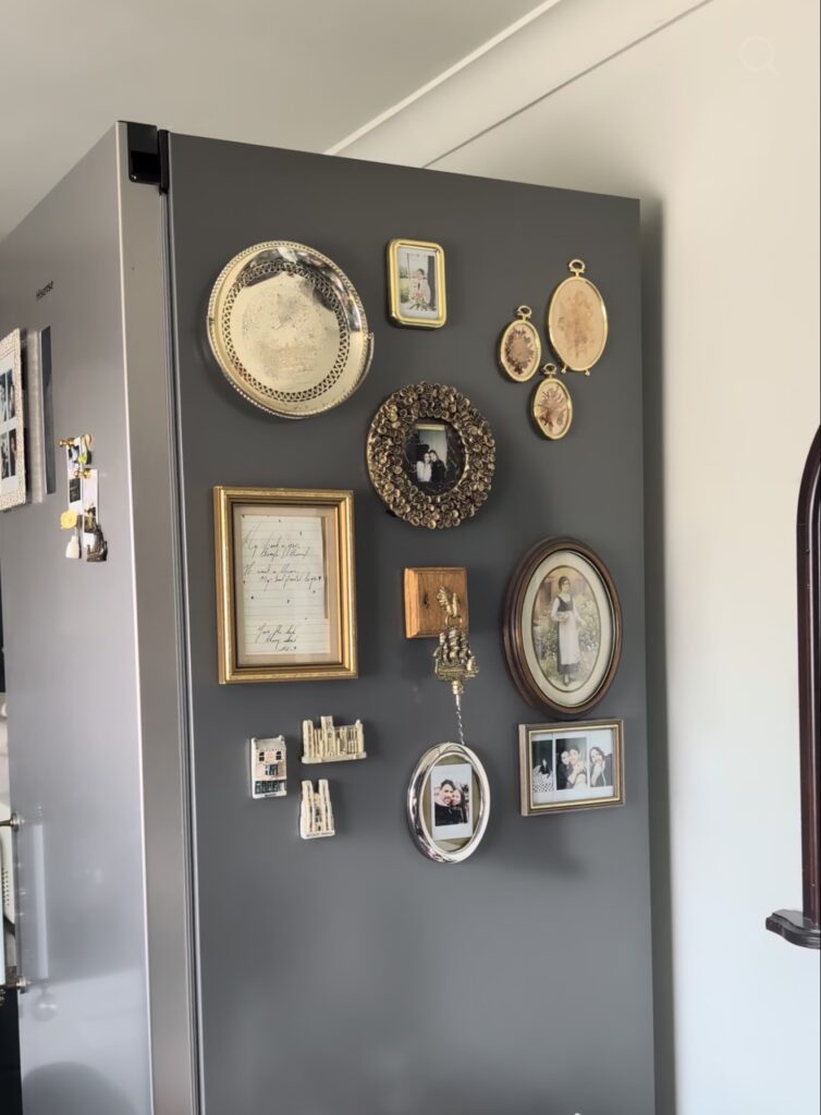 Collected fridge gallery wall on a gray refrigerator with vintage family photos, botanical art, ornate frames, miniature decorative objects and antique-inspired magnets.