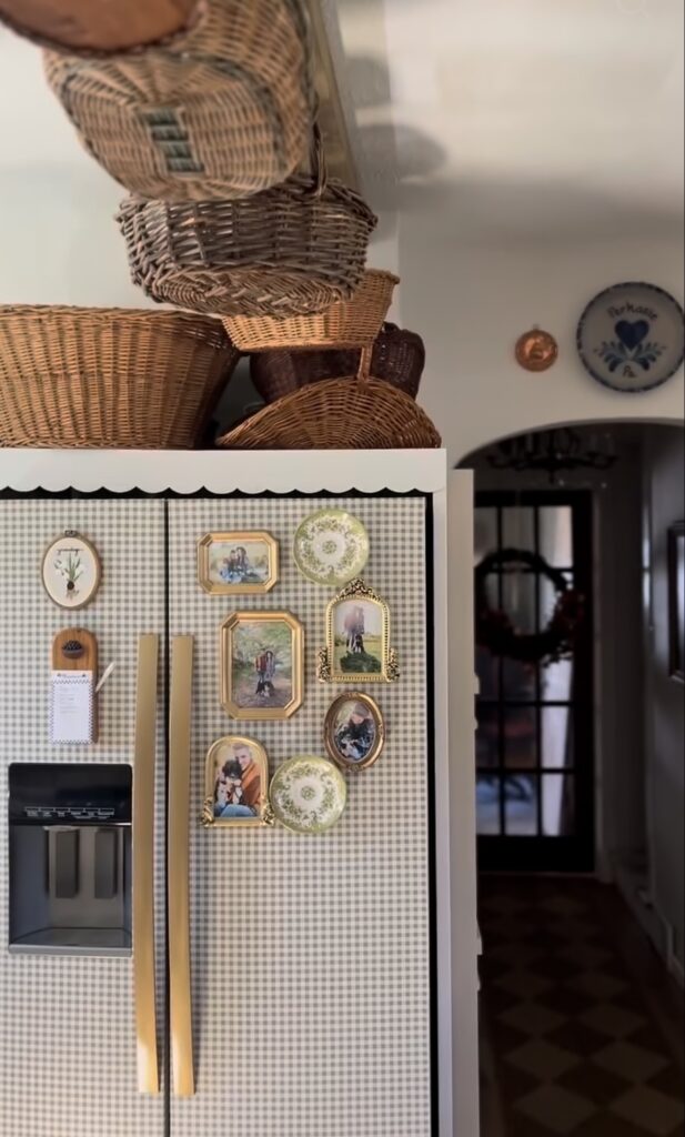 Wallpapered refrigerator with neutral gingham pattern, vintage gold-framed family photos, decorative plates and small artwork arranged as a fridge gallery wall.