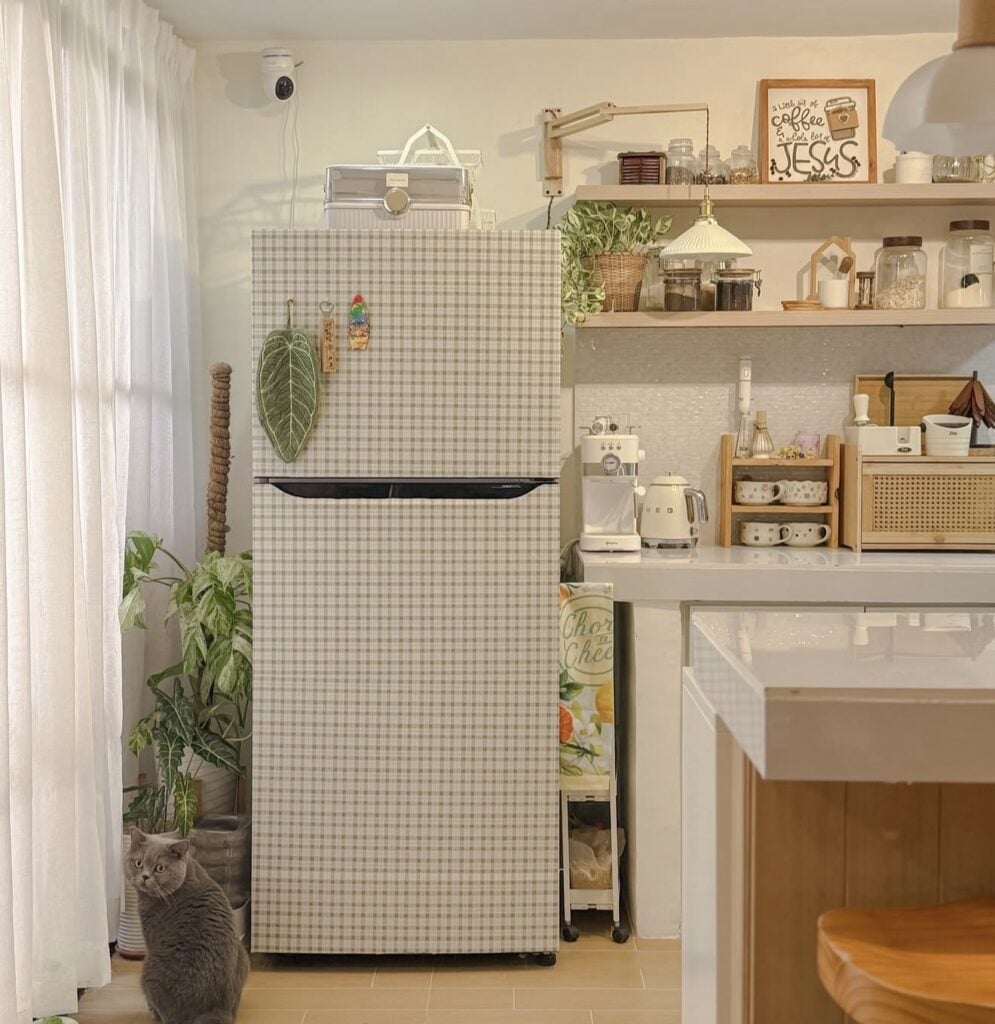 Small refrigerator covered in subtle neutral gingham wallpaper in a cozy kitchen with open shelving.