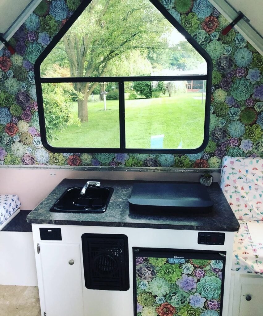 Mini refrigerator in a camper decorated with patterned wallpaper for a personalized interior.