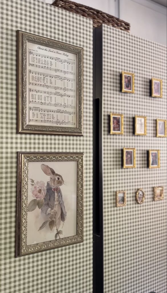 Gingham wallpapered refrigerator decorated with framed sheet music, rabbit artwork and a collection of tiny gold-framed pictures arranged as a fridge gallery wall.