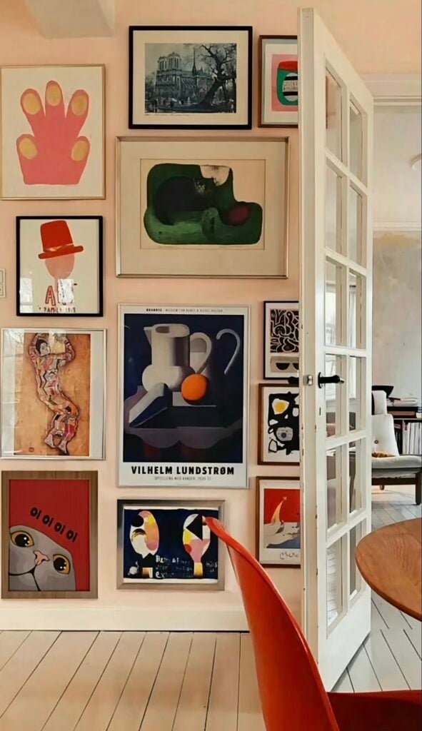 Eclectic floor-to-ceiling gallery wall mixing colorful artwork and cat-themed art in a bright dining area.