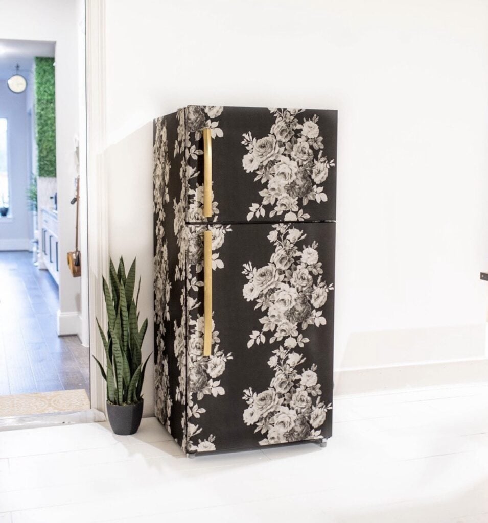 Black refrigerator with dramatic white floral wallpaper and long gold handles.