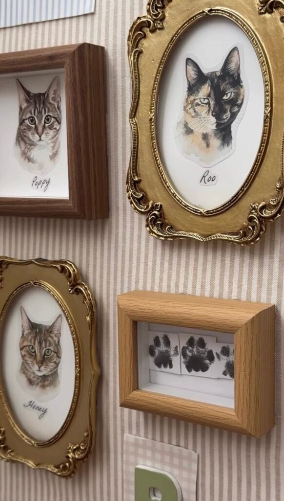 Close-up of a personalized cat gallery wall with framed watercolor portraits of Poppy, Roo, and Honey alongside framed cat paw prints.
