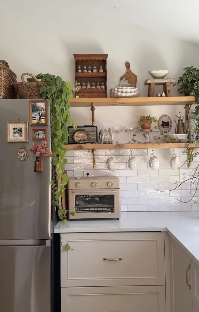 Small fridge gallery wall on the side of a stainless steel refrigerator with family photos, tiny ornate frames and a miniature flower vase beside open kitchen shelving.